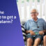 An elderly gentleman, wearing a personal alarm in black, sitting on the sofa in a home setting next to a younger man. Both are happy.