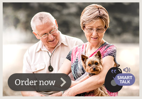 An Australian elderly couple, husband is wearing LiveLife alarm with smart talk feature, wife is holding a dog