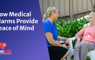 Two ladies smiling at each other, sitting in the garden. The lady on the right wears a medical alarm.